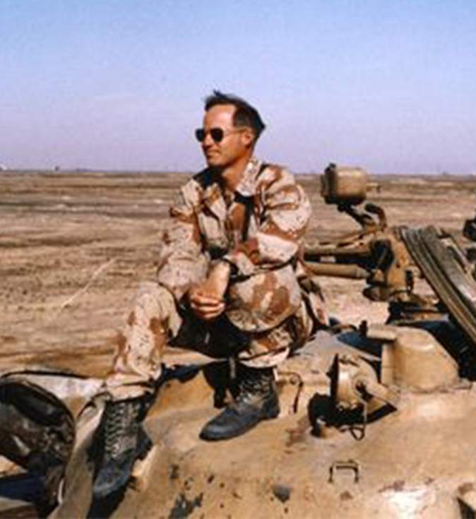 Mike Coffman in U.S. Marine Corps uniform sitting on tank in desert