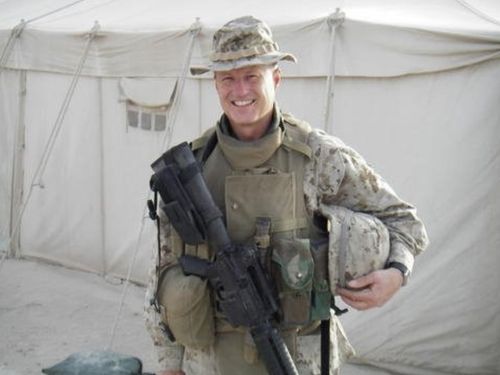 Mike Coffman in U.S. Marine Corps uniform smiling outside tend with military gun