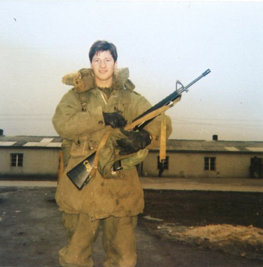 Mike Coffman in U.S. Army greens holding military gun outside in Germany
